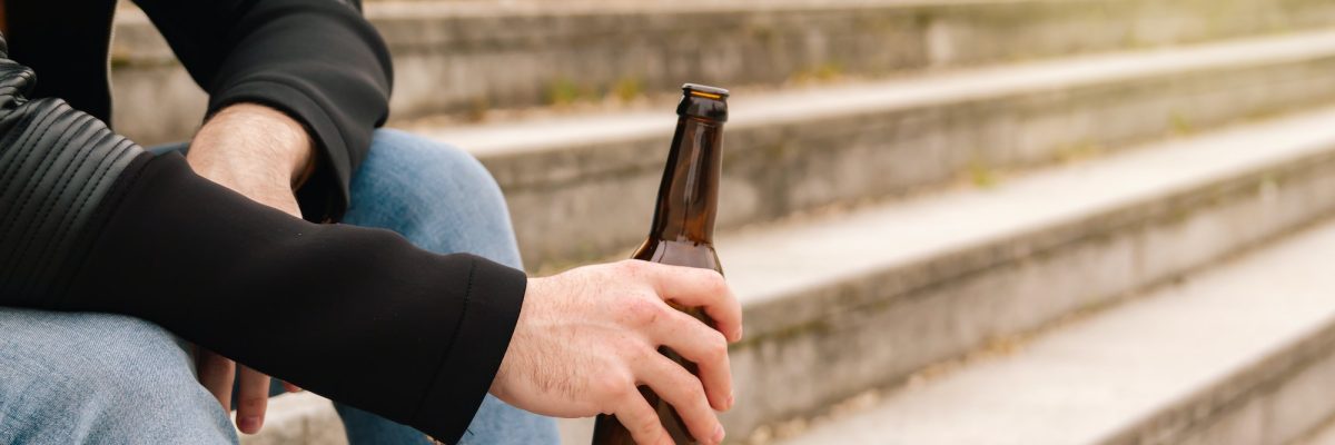Hands of a teenager holding a bottle of beer on the street.