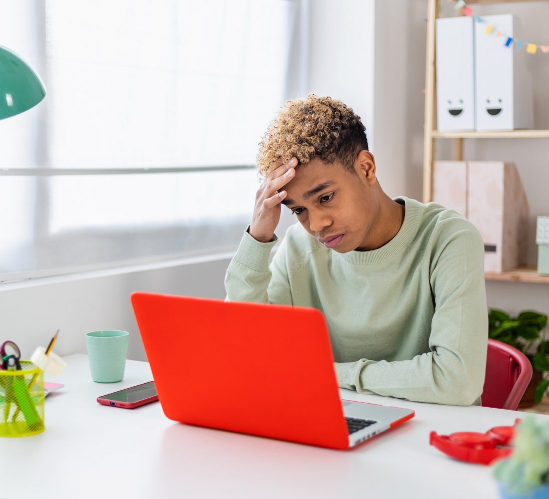 Portrait of stressed teenager boy sitting on desk in youth room